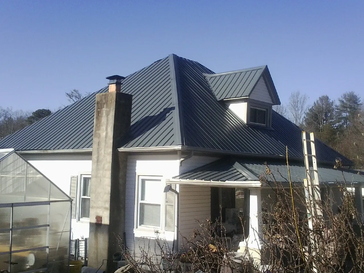 Dark blue standing seam metal roof on a white farmhouse with dormer — Slate & Tile Roof Repair by Roofing Brothers in Loganville
