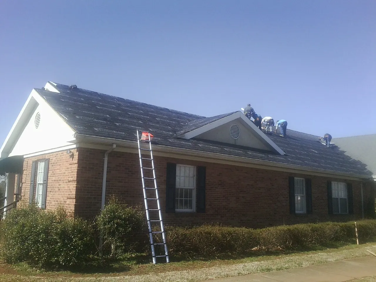 Crew tearing shingles off a brick ranch roof with a ladder set — Emergency Roof Repair work by our crew in Loganville