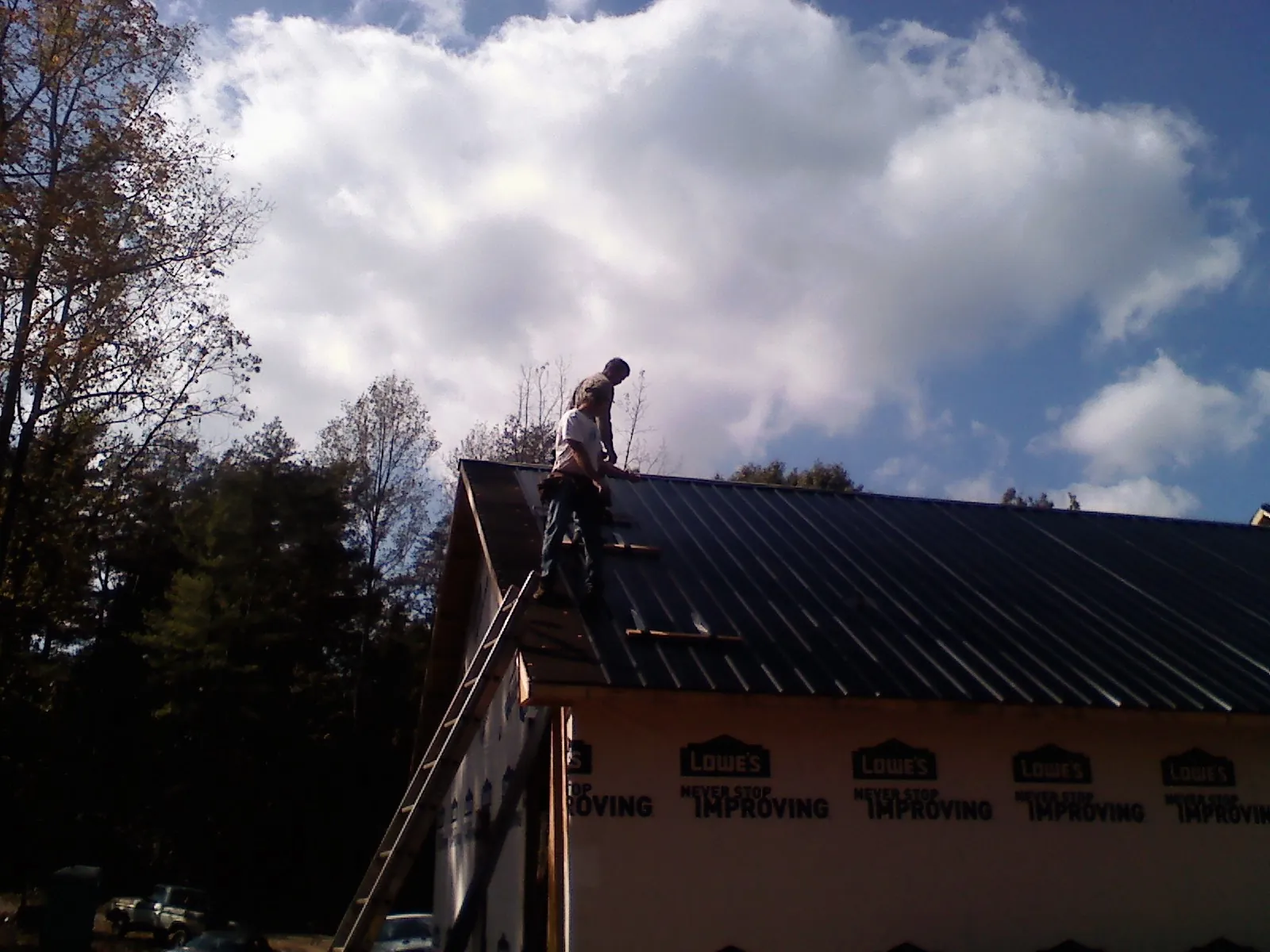 Roofer fastening dark metal panels high against a cloudy sky, from a Roof Inspection job in Loganville